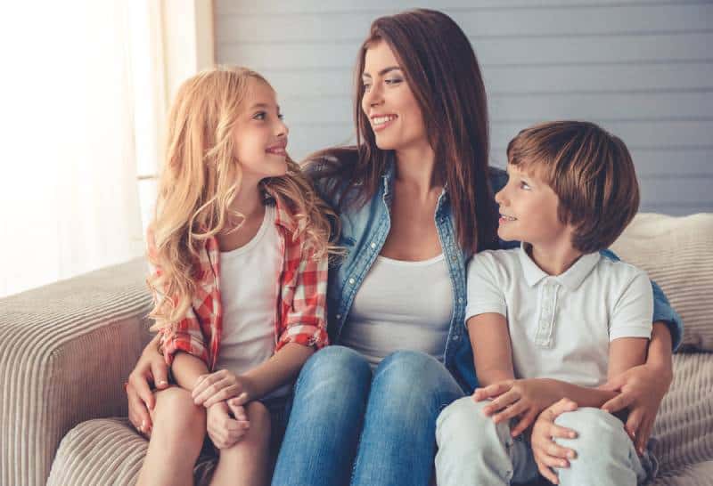 mother and her children are talking and smiling while sitting on sofa