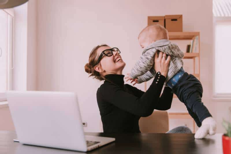 mother playing with little son while working at home with laptop