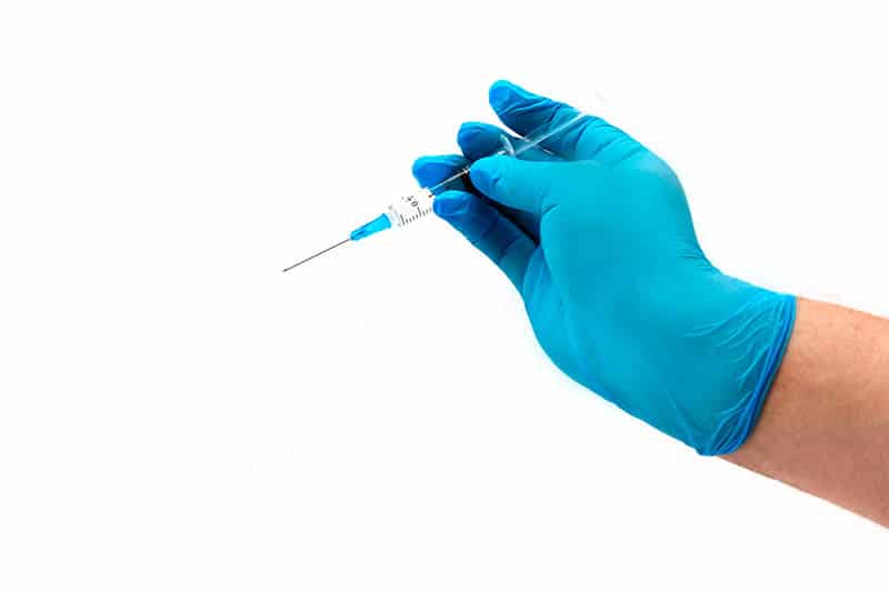 doctor holding a sterile needle in hand with blue gloves on