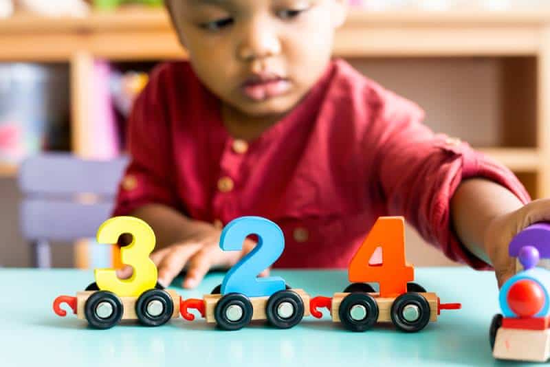 Little boy in red shirt playing mathematics wooden toy at nursery
