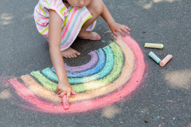 girl drawing a rainbow colored chalk on the asphalt on summer sunny day