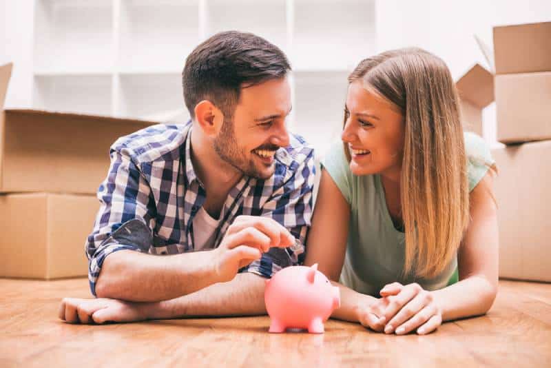 Young couple lying on floor and putting money in a piggy bank
