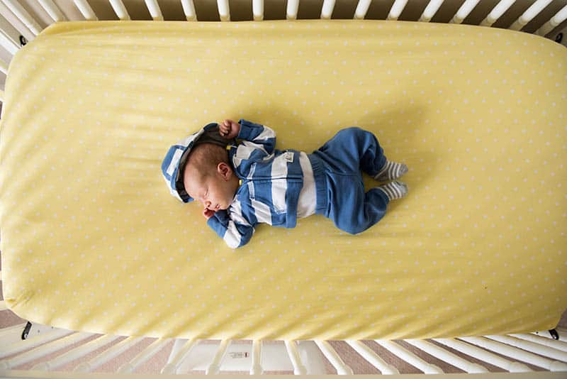 baby in crib with yellow crib sheet