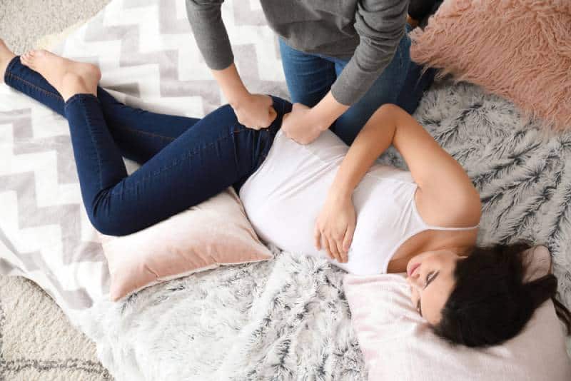 Doula massaging a pregnant woman while she is lying on a bed in her room