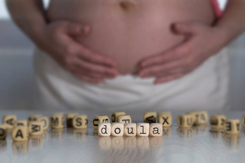 Doula written on wooden letters with pregnant woman holding her tummy in the background