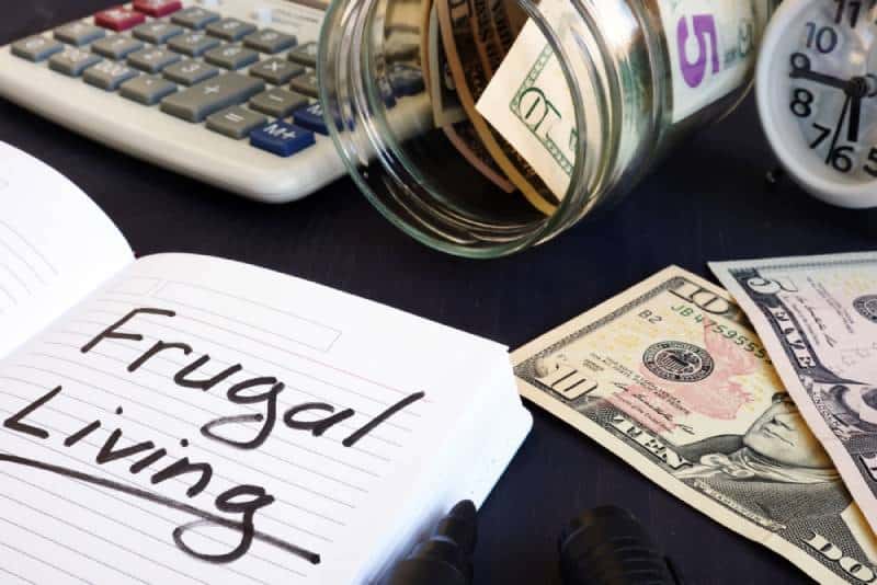 Frugal living written on a note pad, money and a calculator on a table