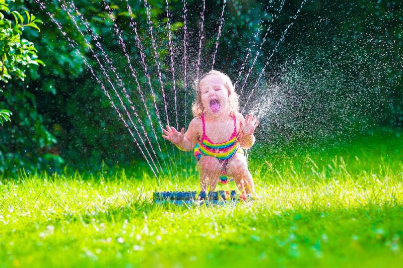 Kid in bathing suit playing with sprinkler in garden in summer