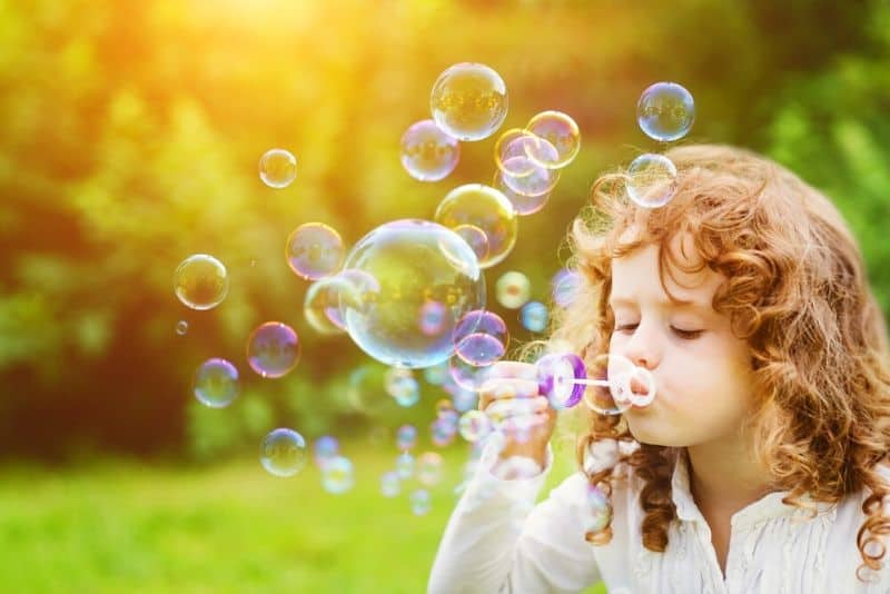 Little girl blowing bubbles on the green meadow in spring time