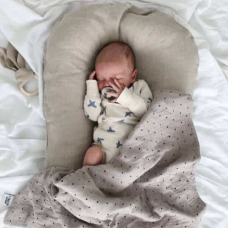 Newborn baby boy sleeping in a grey cotton baby lounger on white sheets