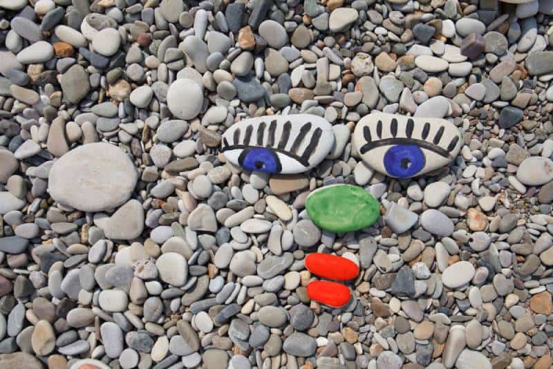 Sea smooth stones, pebbles with human face, stone painting on the beach as background