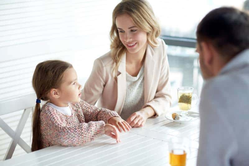 Happy mother, father and little girl having dinner and talking at restaurant 