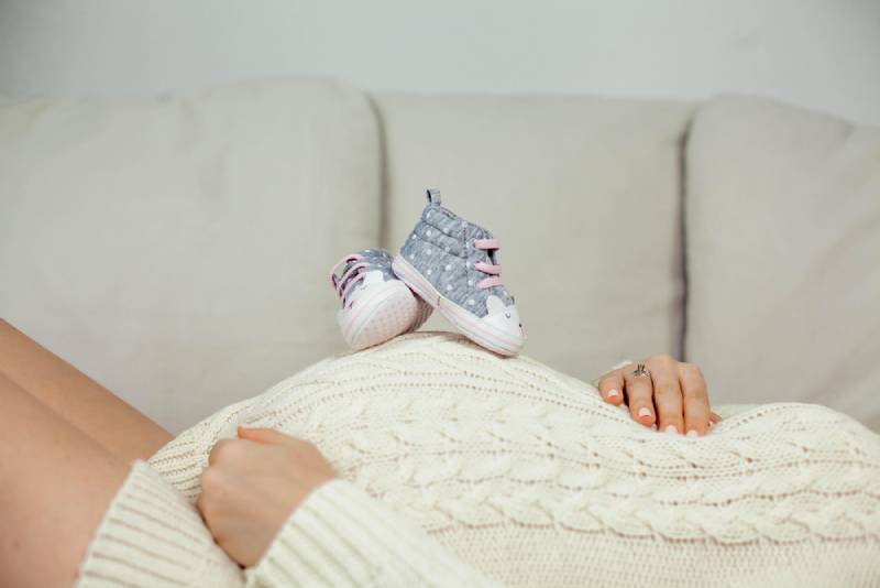 Pregnant woman lying on sofa with a pair of shoes on her belly