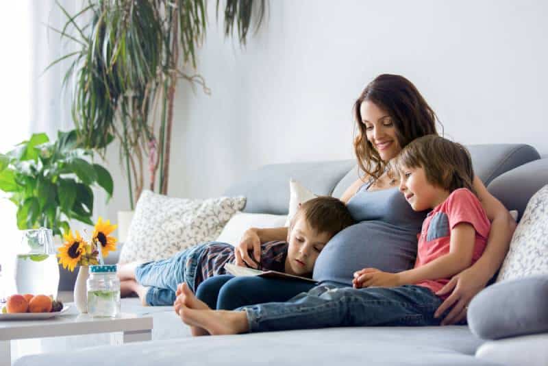 Pregnant woman, reading a book , at home to her two boys, eating fruits, hugging and laughing