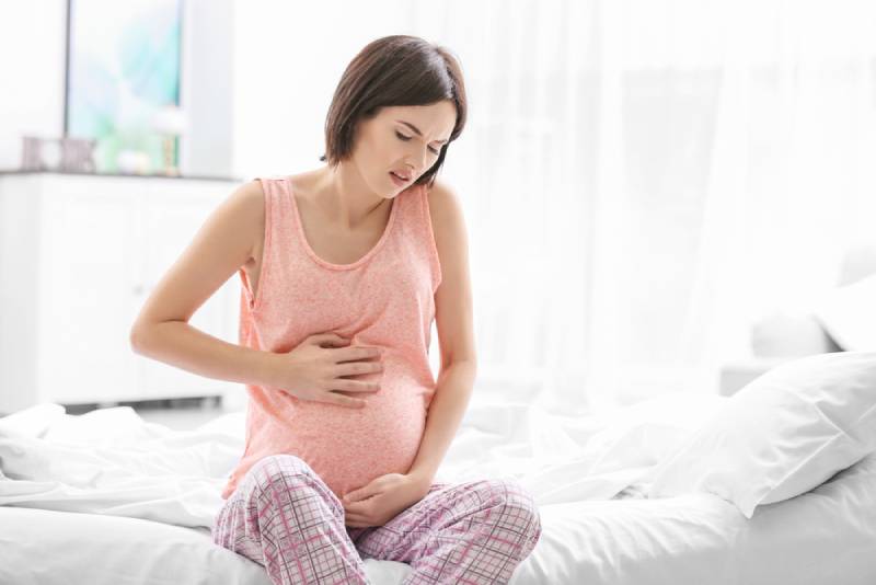 Pregnant woman sitting on bed and holding her tummy because of pain