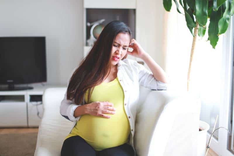 Pregnant woman in third trimester sitting on sofa and having tummy pain