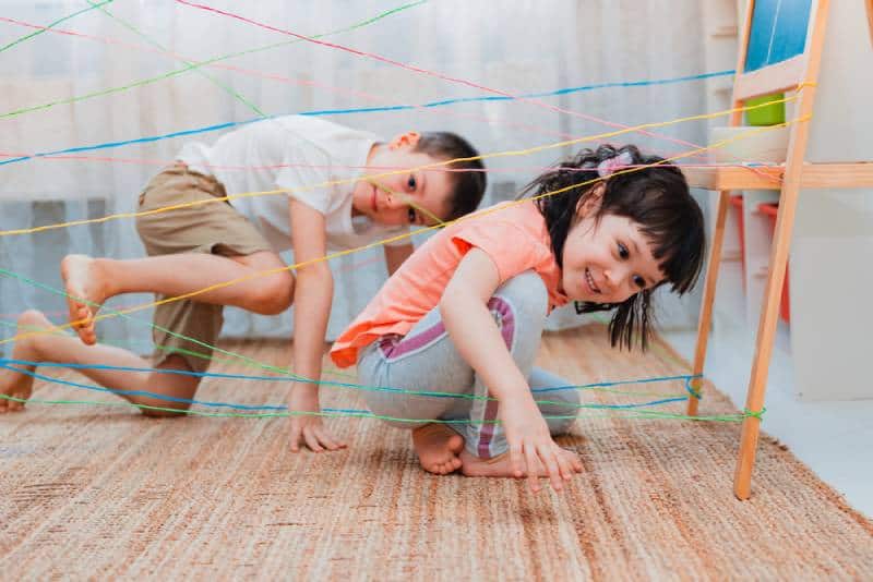 little girl and boy playing a game with colorful ropes
