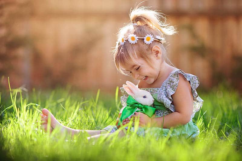 little girl in a dress sitting on the grass and playing with a bunny