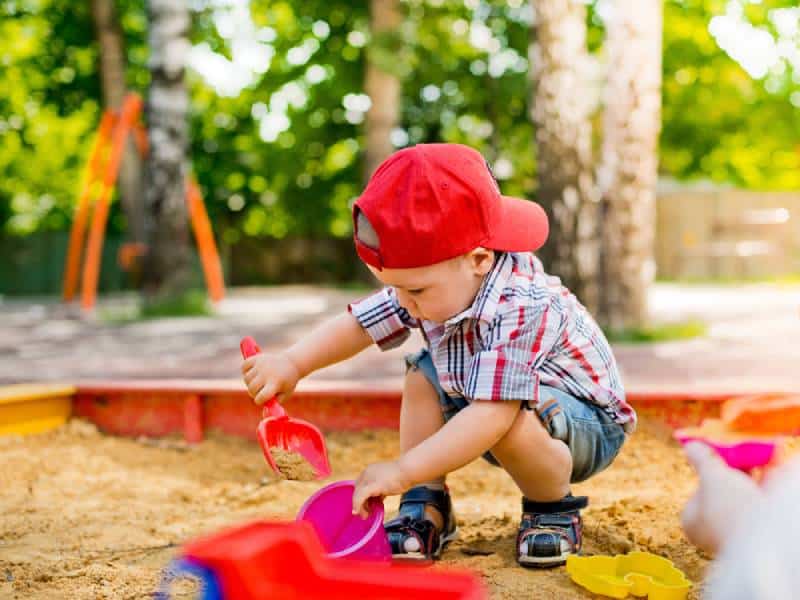 Toddler playing in sandbox with toys outdoors in summer