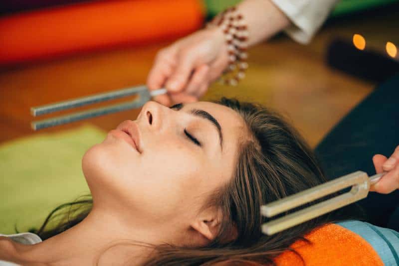 Woman lying with her eyes closed at sound therapy next to tuning fork 