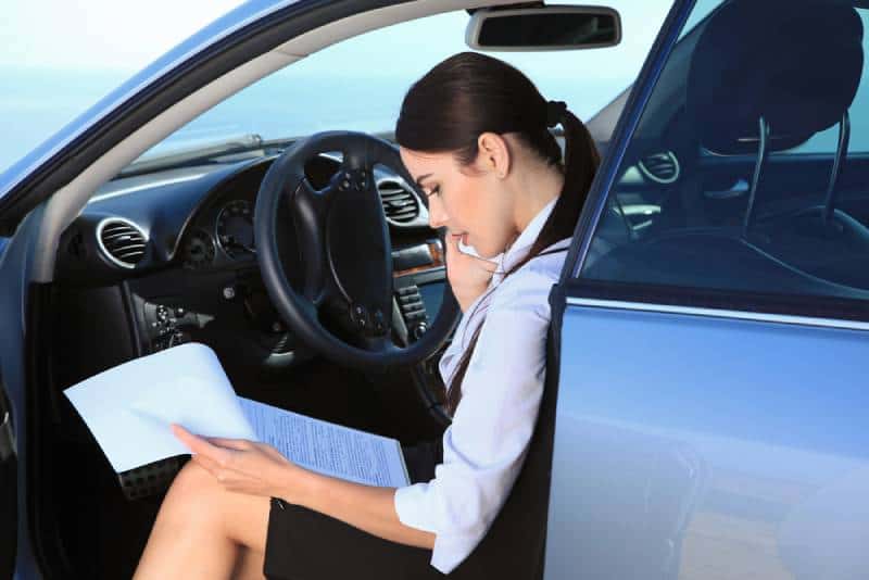 Business woman in the car examines important documents while talking on the phone