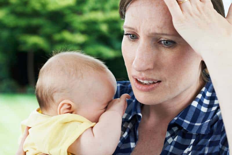 Woman holding a baby in yellow shirt and holding her head because she forgot something