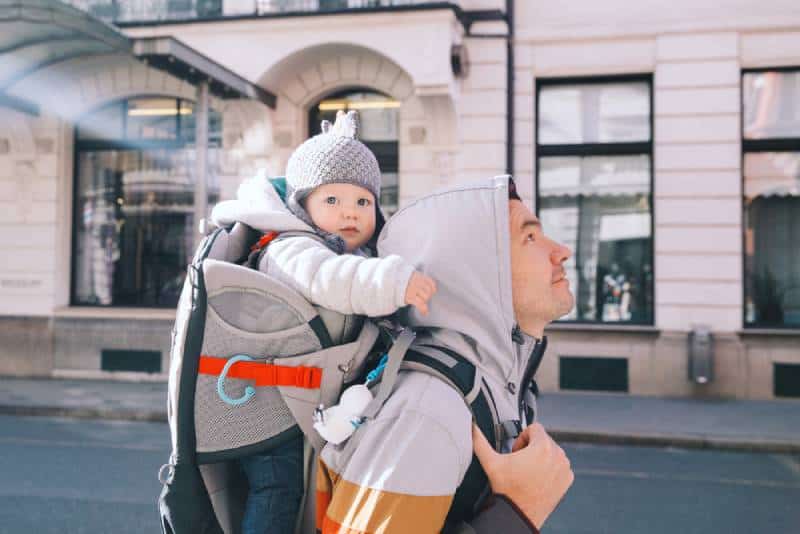Father with child son in carrier backpack walking down the street in daytime