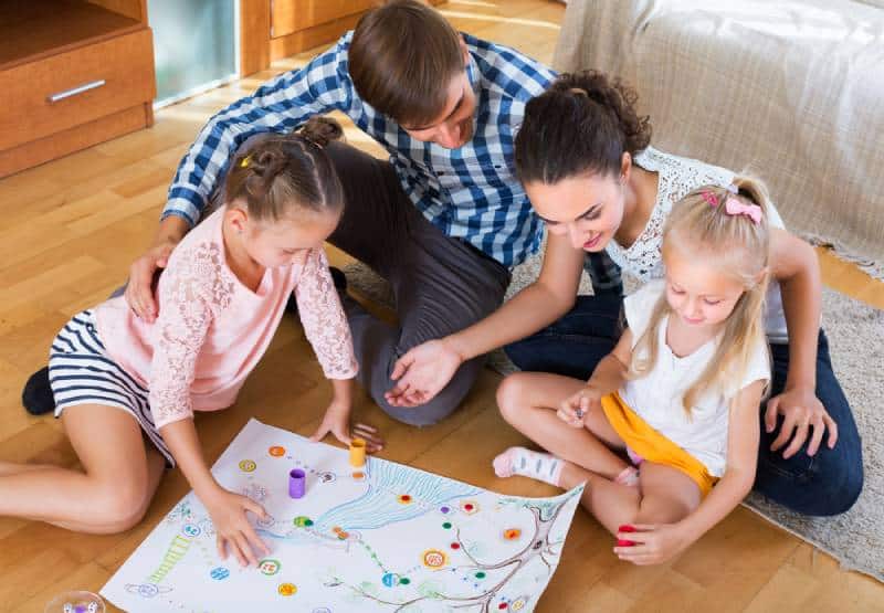 Happy young family with 2 kids playing at board game in domestic interior