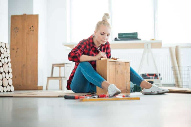 Young woman repairing furniture at home, sitting on the floor, DIY concept