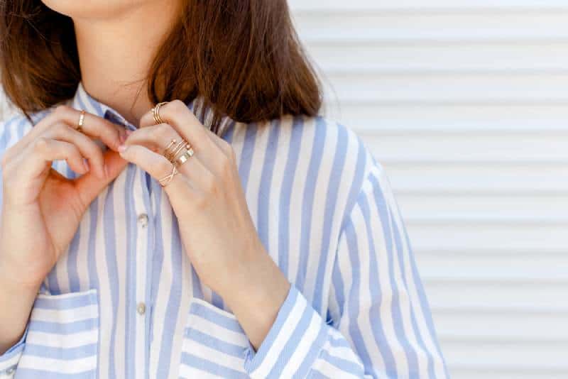 Stylish woman wearing blue striped shirt buttoning a button, wearing jewelry