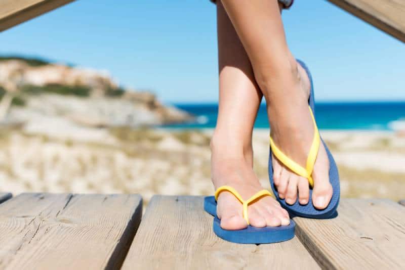 Low section of woman wearing yellow blue slippers while standing on board walk