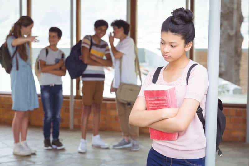School friends bullying a sad girl in corridor at school