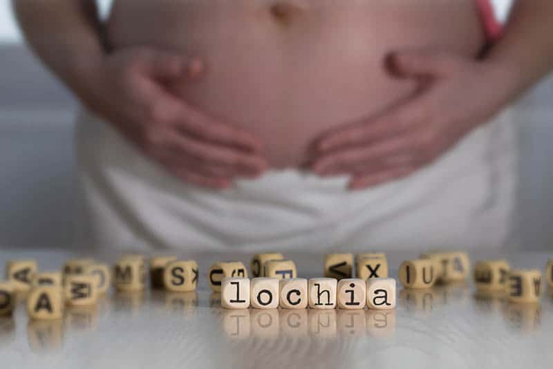 Word LOCHIA composed of wooden letters. Pregnant woman in the background