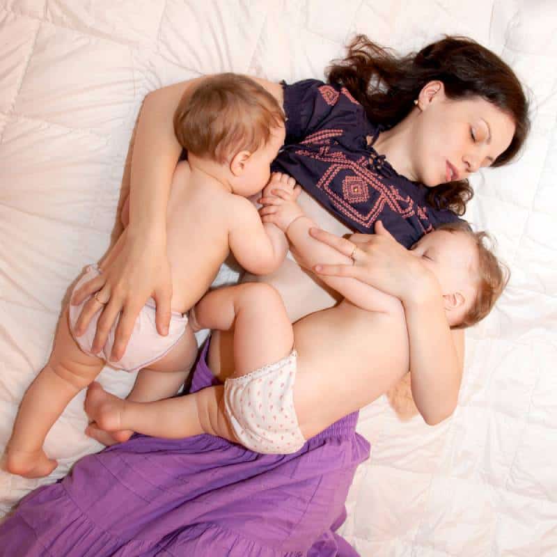 Mom breast feeding two little sisters twin baby girls at the same time