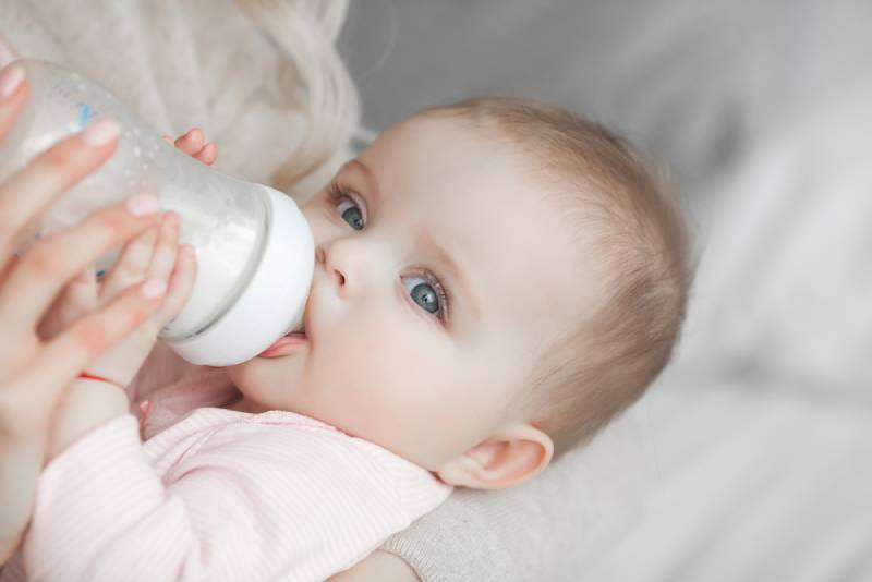 mother feeding her little cute baby daughter with bottle of child formula