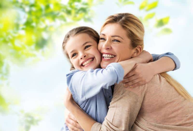 happy smiling mother hugging daughter over green natural background