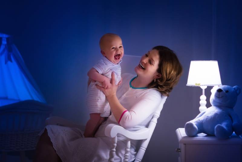 Mother and baby reading a book and having fun before bedtime in dark bedroom