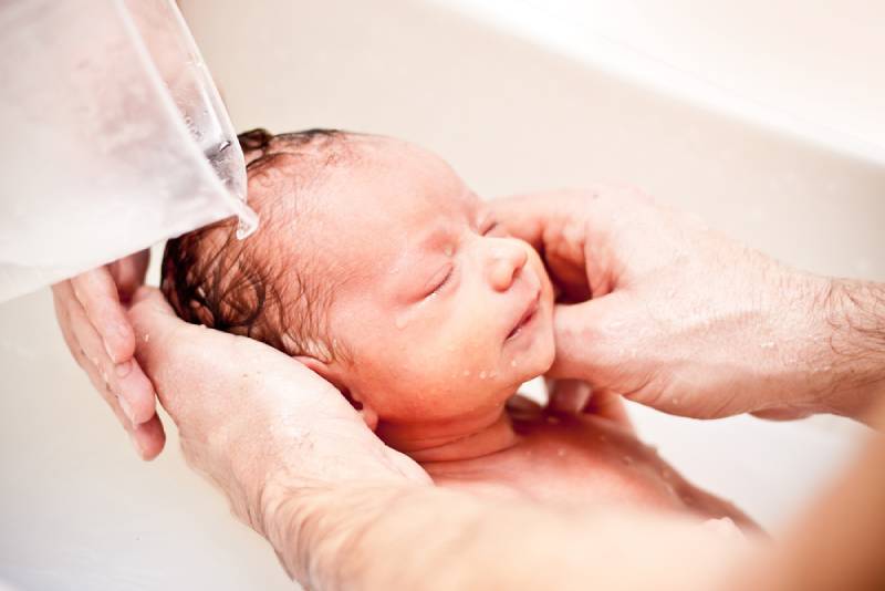 Small baby first bathing on father hands, while he is pouring water on his head