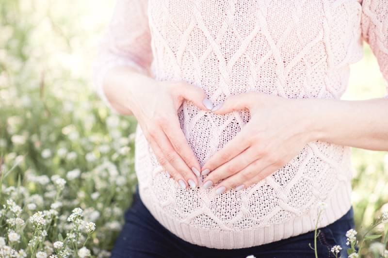 Pregnant woman making heart with fingers on her tummy outdoors
