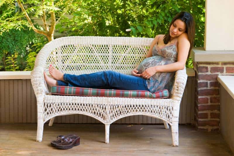 A beautiful young pregnant woman in jeans and colorful blouse relaxing outside white waiting for the birth of her baby