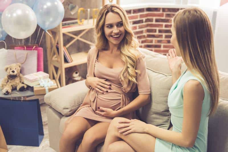 pregnant woman and her friend are talking and smiling while celebrating baby shower at home