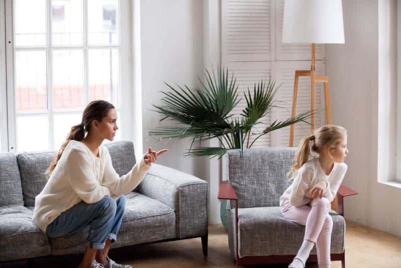 Strict mom scolding stubborn sulky kid girl in living room at home while she doesn't want to talk