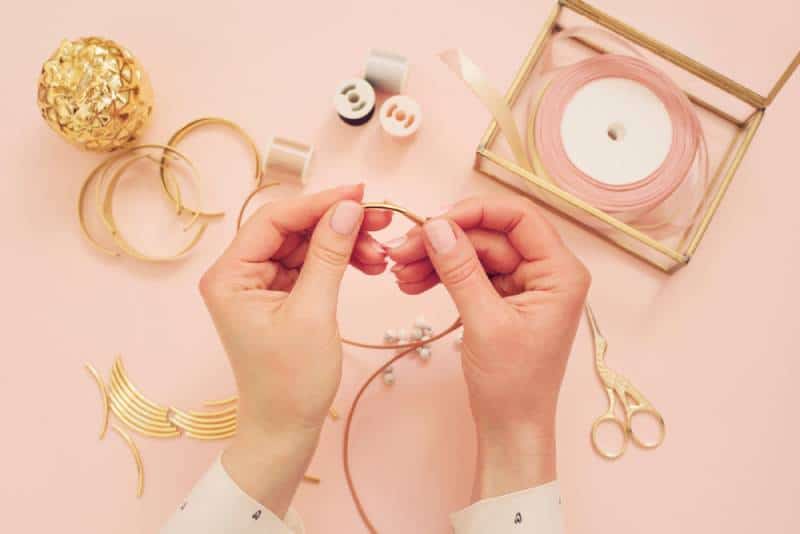 Woman hands making handmade jewelry on pink background