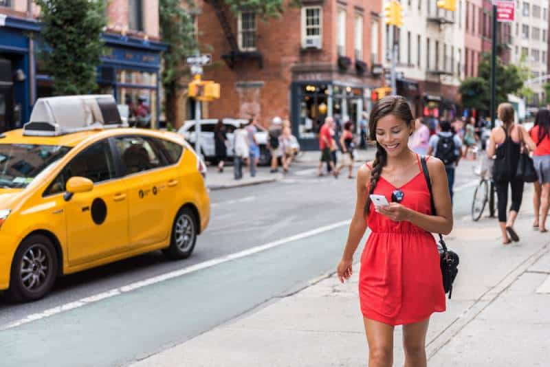 Woman in red dress walking in new york city and using her phone 
