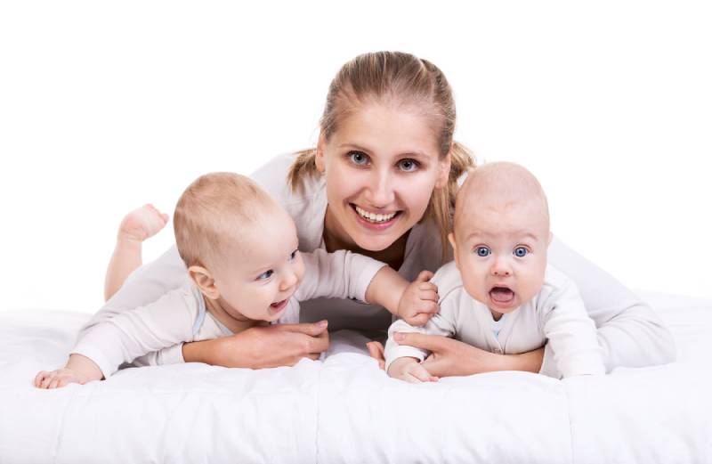Happy woman in white lying on bed with her cute twins