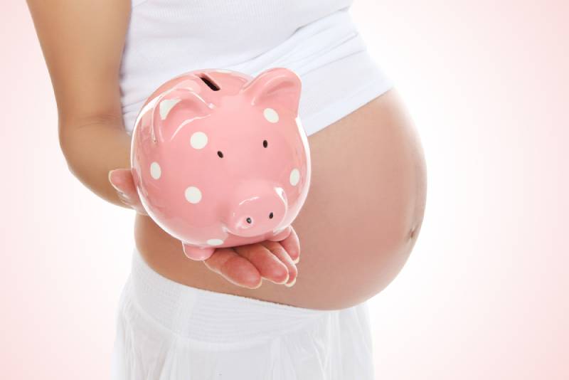 A pregnant mom in white to be holding a piggy bank