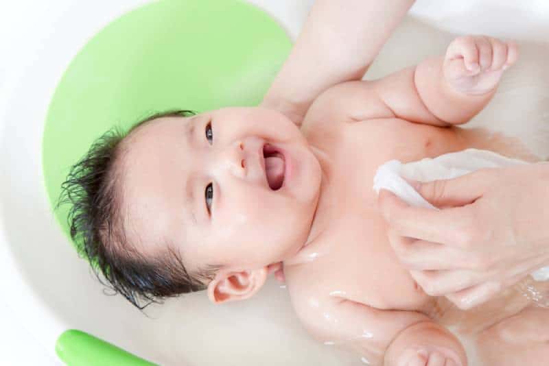 Mom bathing a newborn baby in a tub while he is smiling