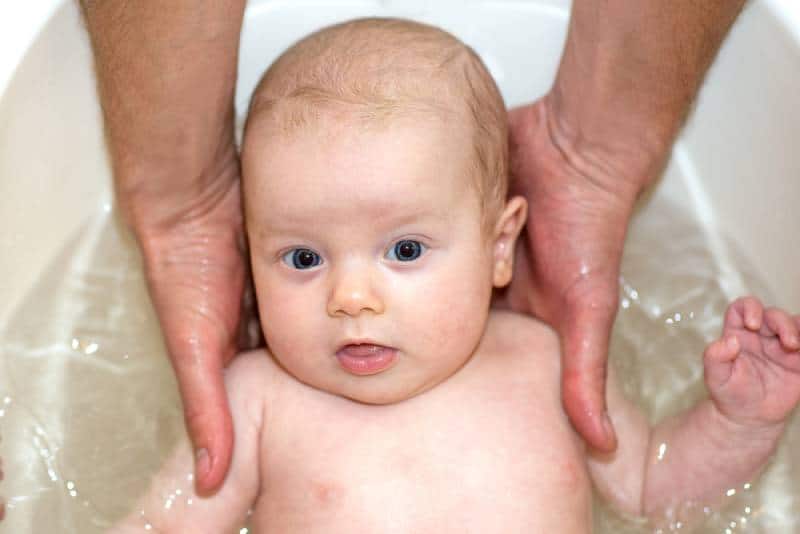 Bathing baby in the bath while dad's hands support the baby's head