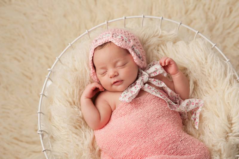 A portrait of a five week old newborn baby girl wearing a pink bonnet and lying in a basket