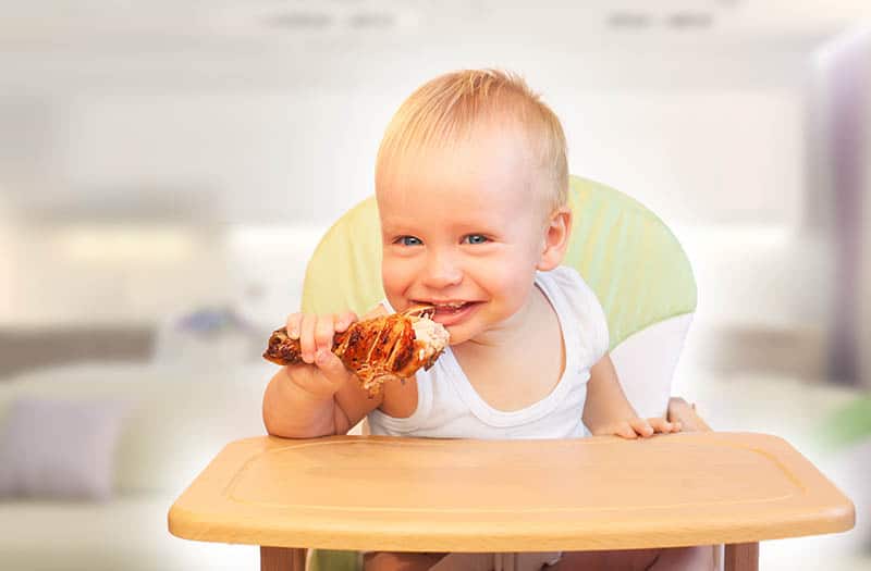 baby eats meat while sitting in high chair