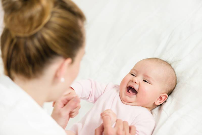 Laughing baby looking at mom and playing with her